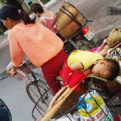 Em bé đang ngủ ngon trên chiếc xe đạp cà tàng của mẹ giữa phố 11